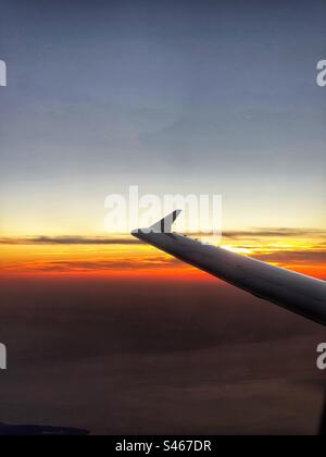 Silhouette of the wing of a holiday jet in flight against a colourful sunset sky. Travel concept. Stock Photo