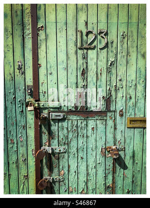 Paint peeling off an old green door number 123 Stock Photo