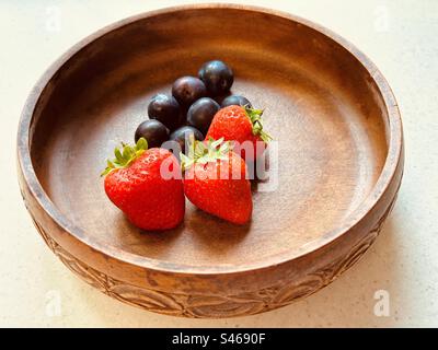 Three strawberries and seven plums in a circular wooden bowl. Fresh, colourful, juicy, sweet, nutritious, summer fruit. Stock Photo