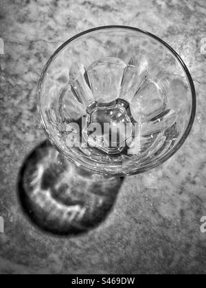 An overhead view of a small drinking glass. An interesting shadow is created by the use of a spotlight shining on a marble restaurant table. Photo ©️ COLIN HOSKINS. Stock Photo