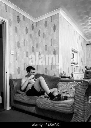 A teenage boy sat on a sofa in the evening eating a bowl of cereal. Stock Photo