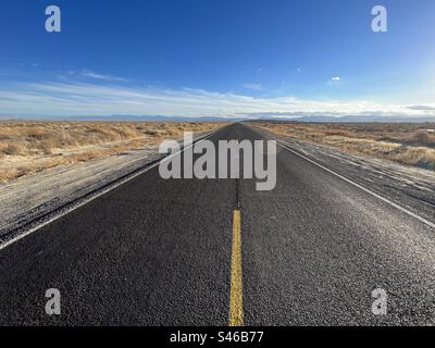 Fresh black asphalt with bright yellow markings on highway through the desert in Southern California. Blue sky overhead Stock Photo