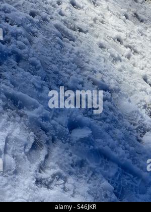 Strong winter sunlight and abstract patterns on snow in California mountains, creating a textured winter background in portrait format Stock Photo