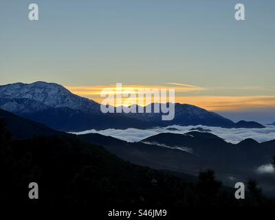 Mountains with low clouds rolling in below the silhouetted peaks at sunset Stock Photo