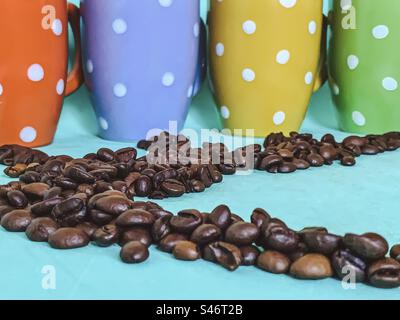 Coffee beans and coloured, polka dot mugs. Stock Photo