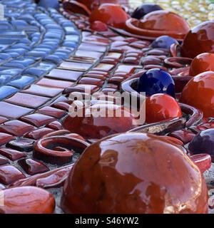 Square, closeup of blue and red ceramic shapes, with glazed red, yellow and blue tiles, part of an outdoor installation, seen in overcast light Stock Photo
