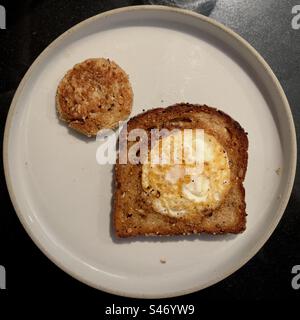 Fried egg in a circular hole in fried bread, with the cut-out hole also fried, served on grey plate Stock Photo