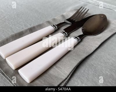 White handled cutlery (knife, fork, and spoon) on green napkins with green tablecloth Stock Photo