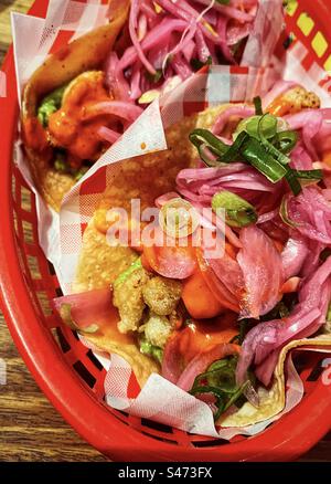 High angle view of fried cauliflower with pickled onion, tomato salsa and guacamole on soft tortilla in red basket on table. Vegan/vegetarian tacos. Mexican food. Stock Photo