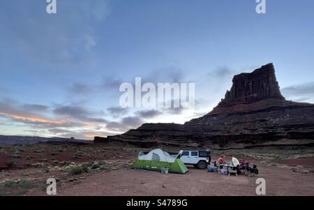 Campers set up their campsite at the base of Airport Tower, a formation along the White Rim Trail in Canyonlands National Park.  Campers are required to camp at designated campsites and need permits. Stock Photo