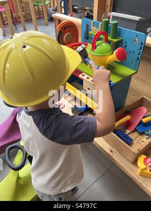 Educational play - young boy wearing a yellow hard hat playing with wooden work bench Stock Photo