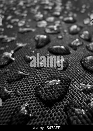 Macro closeup of water drops on black vinyl reflecting bright sunlight. Stock Photo