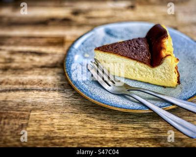 Close-up of a slice of Basque cheesecake on a plate with two forks on wooden table. Stock Photo