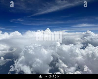 Wide aerial, cumulus clouds below, cirrus clouds with deep blue sky above, seen through aircraft window Stock Photo