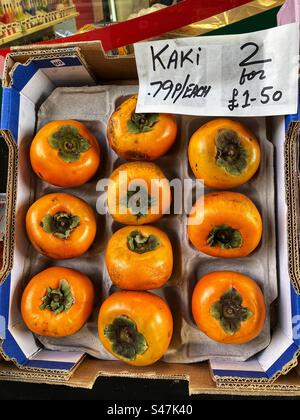 Kaki or Persimmon priced up for sale at Grocers shop Stock Photo