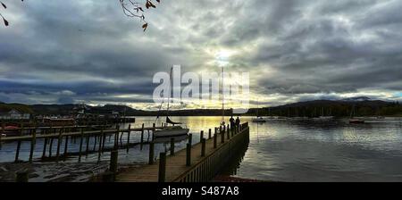 Looking over Windermere at dusk from Waterhead, Ambleside with a couple of people standing on the jetty - Lake District U.K. Stock Photo