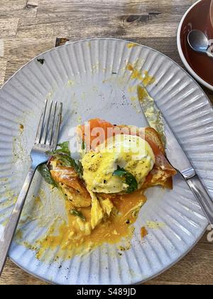 Directly above close-up of partly eaten eggs Benedict with smoked salmon, hollandaise sauce and spinach leaf on shokupan/ Japanese milk bread on plate with cutlery on table. Stock Photo