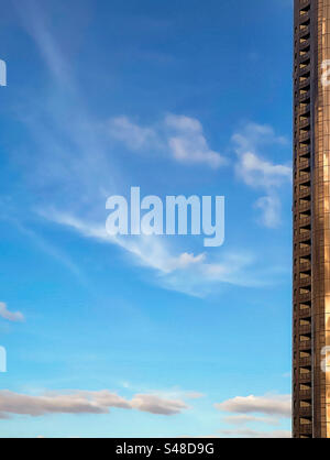 Low angle view of skyscraper on blue sky with a few swirling white clouds on a sunny afternoon with copy space. Abstract. Tranquility. Modern. Stock Photo
