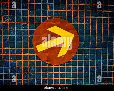 yellow arrow in a brown circle is pointing up right direction against a tiled wall Stock Photo