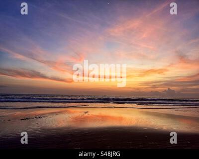 Sunset at Seminyak beach Bali with the sun set over the sea and the orange glow remaining in the clouds and the orange light reflecting in the shallow water Stock Photo