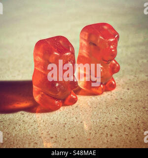 orange couple gummy bear candy single orange gummy bear candy gel in orange transparent translucent color on a simple white worktop in a store shop with a ray if lights on them Stock Photo