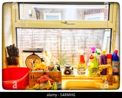 A kitchen window in the morning sun with cleaning products washing up bowl knife block scales and candle Stock Photo