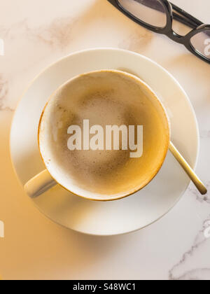 Empty Cappuccino coffee cup and spectacle’s on a mable table Stock Photo