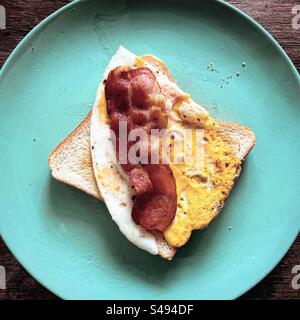 too view of fried egg on toasted bread with a slice of fried baked pork bacon for breakfast in green plate Stock Photo