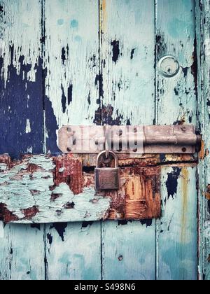 Old lock on a battered and weathered wooden door with peeling and faded paint. Stock Photo