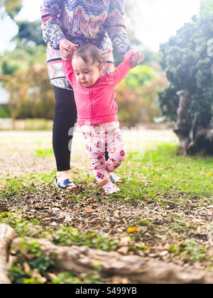 Baby’s first steps outdoors. Baby walking with being helped by adult Stock Photo