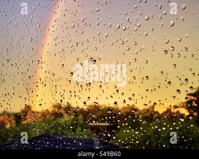 Rainbow in sunset sky seen through raindrops on window. Stock Photo