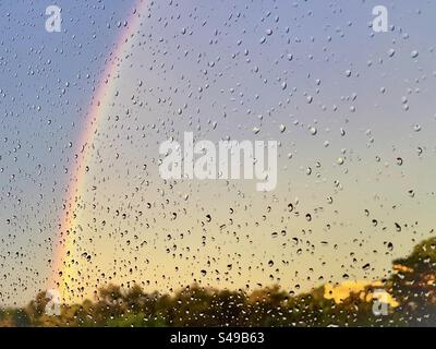 Rainbow in sunset sky seen through raindrops on window. Stock Photo