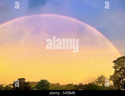 Rainbow in sunset sky after a storm, arching over trees below, seen through wet window glass. Stock Photo