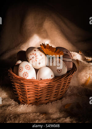 A basket of decorated eggs with a yellow flower, on a white, soft and shadowy background Stock Photo
