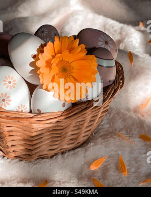 Basket of decorated eggs and pot marigold flower on soft white blanket Stock Photo