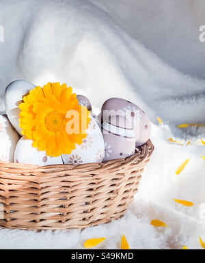 A yellow pot marigold flower in a basket of decorative eggs on a soft, white blanket Stock Photo