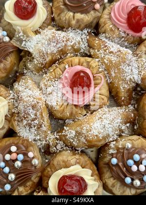 Close-up image of assorted Baklava and Saragli traditional Greek and Turkish sweets topped with cherries and coconut flakes, displayed in Athens, Gree Stock Photo