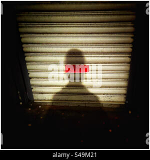 Shadow on shop shutters with red light shining through slot Stock Photo