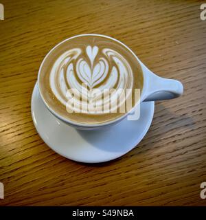 Latte coffee with attractive pattern in the cream on top, white ceramic cup on wooden table Stock Photo