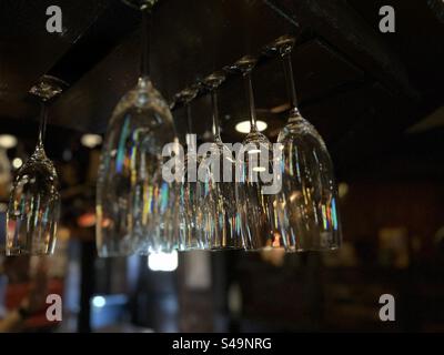 Shallow focus view of sparkling, clean Champagne glasses hanging from a rack in a bar, dark background Stock Photo