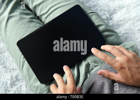 Close up of a young man on the sofa touching the black screen of a digital tablet. Person works on a tablet at home. Lying man holds a tablet and star Stock Photo