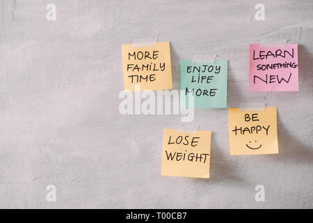 Group of New year Resolution Notes on pink, yellow, orange and green on wall written with  message of more family time, lose weight and be happy Stock Photo