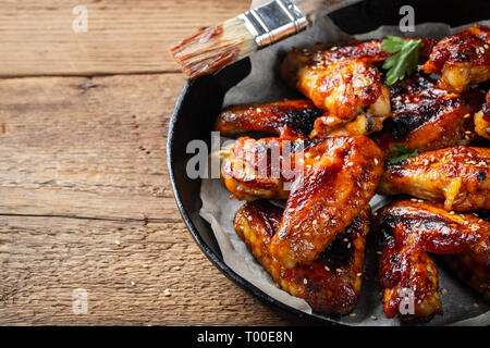 Baked chicken wings in barbecue sauce in a cast iron pan on an old wooden rustic table. Stock Photo