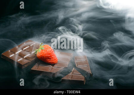 Broken chocolate bar with strawberry isolated on black in smoke Stock Photo