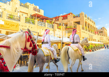 Doha, Qatar - February 20, 2019: heritage Police Officers in traditional 1940s Qatari uniform at old Souq Waqif riding white Arabian Horses on Stock Photo