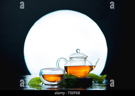 Asian tea ceremony still life header with a full moon. Glass tea bowl and teapot against a shining circle. Stock Photo