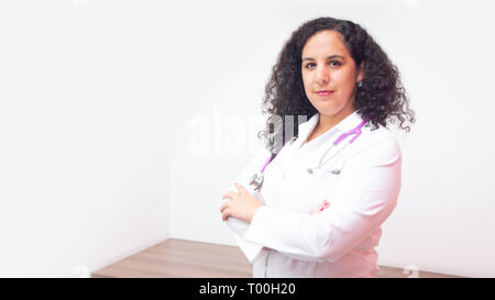 Latin female doctor with serious attitude standing looking towards the camera in her office with stethoscope on her neck with her arms crossed Stock Photo