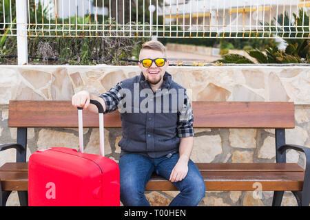 Travel, tourism and people concept - happy man sitting on a bench with suitcase, he is ready for travelling Stock Photo