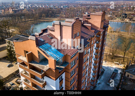 Aerial view of new tall apartment building in quiet area on background of developing city landscape under bright blue sky. Stock Photo
