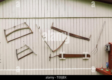Antique saws, pitchfork and other hand tools hanging on the side wall of old grey painted wooden planked barn in residential backyard Stock Photo
